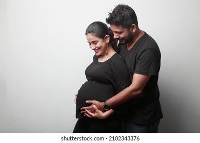 Young Couple Of Indian Ethnicity Expecting Baby Standing Together Indoors
