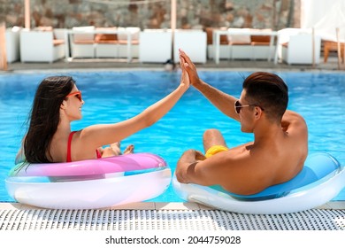 Young couple with inflatable rings giving each other high-five in swimming pool - Powered by Shutterstock