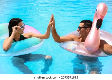 Young couple with inflatable rings giving each other high-five in swimming pool - Powered by Shutterstock