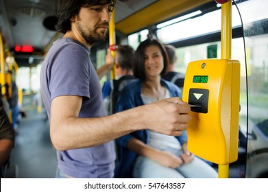 Young couple in inside of the city bus. The girl sits and transfers to the guy tickets. The young man inserts the ticket into the validator. - Shutterstock ID 547643587