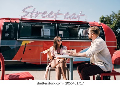 Young couple interacting while having fast food in outdoor cafe against street truck - Powered by Shutterstock