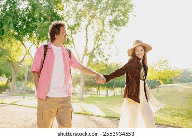 A Young Couple Joyfully Walking Hand in Hand Through a Beautiful Sunlit Park Together - Powered by Shutterstock