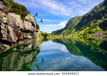 Young couple jump together into lake in mountains with beautiful blue water and reflexion. 
