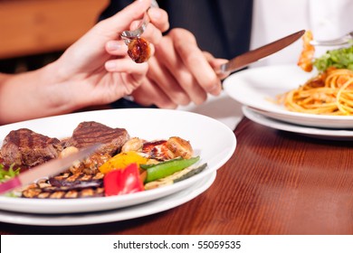 Young couple (just hands to be seen) enjoying dinner, he has some noodles while she is eating a good steak