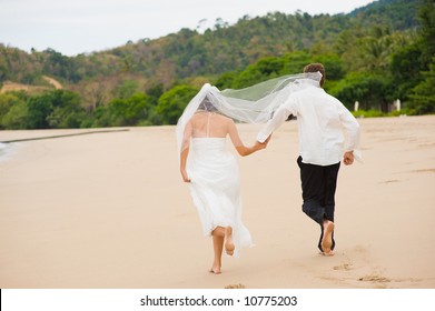 A Young Couple Just Married On The Beach Running Away