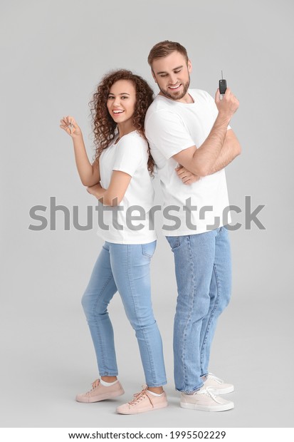 Young couple with key from car and home on\
grey background