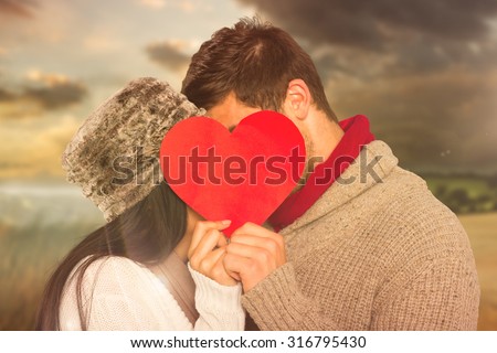 Young couple kissing behind red heart against country scene