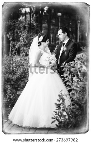 Young couple kissing in wedding gown. Bride holding bouquet of flowers.