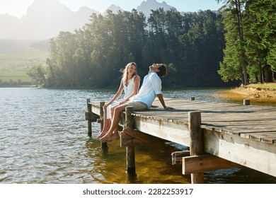 Young couple, lake and jetty with laughing, happiness and bonding with love in nature for holiday. Man, woman and comic joke on bridge by water to relax with conversation, care and vacation in summer