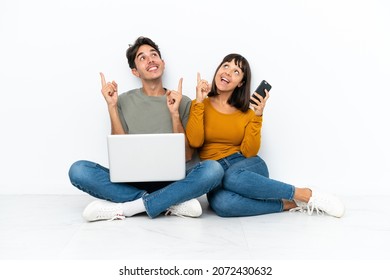 Young couple with a laptop and mobile sitting on the floor pointing with the index finger a great idea