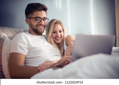 Young Couple With Laptop On Bed.Man And Woman Enjoying Watching Video On Laptop While Relaxing In Bedroom.