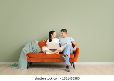 Young couple with laptop relaxing on sofa near color wall