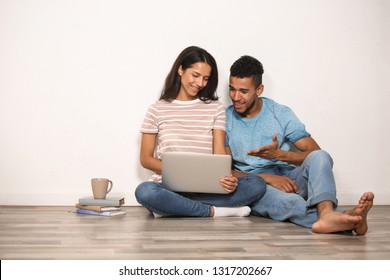 Young couple with laptop sitting on floor near light wall