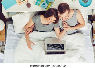 Young couple with laptop watching movie in bed