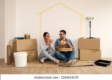 Young couple laughing while sitting on the ground making a break from moving-in and holding slice of pizza in their hands. - Powered by Shutterstock