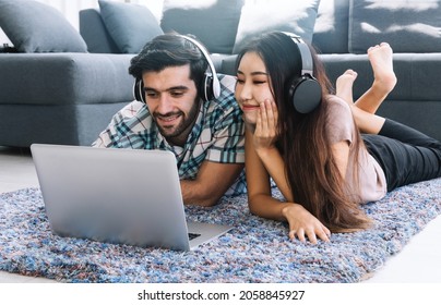 Young Couple Laying On Floor Listen Music With Headphone And Using Laptop At Living Room.