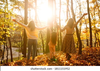 A Young Couple Of Lesbian Ladies Walking In The Autumn Forest. The Homosexual Family Playing With Her Daughter In The Autumn Park At Sunset.