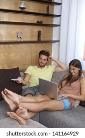 Young couple in living room, girl browsing internet on laptop, guy watching tv.