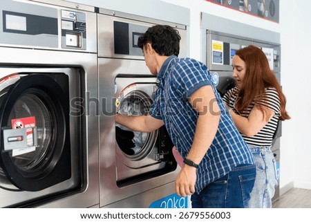 Young couple loading clothes into washing machine at a self-service laundromat, doing laundry and using shared appliances