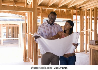Young couple looking at blueprints in partially built house, smiling