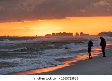 Young couple looking at dramatic magical orange red sunset in Santa Rosa Beach, Florida with Pensacola coastline coast skyline in panhandle with ocean gulf mexico waves