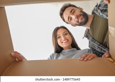 Young Couple Looking Inside Of Cardboard Box With Belongings After Moving Into New House