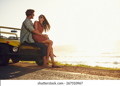 Young couple looking into each other's eyes. Romantic young couple sitting on hood of their car enjoying the moment, outdoors with copy space. Young couple in love on a road trip.