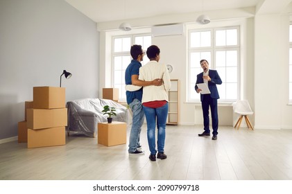 Young Couple Looking At Their Modern, Big, Spacious Future Apartment. Boyfriend And Girlfriend Or Husband And Wife Planning To Buy New Home, Meeting With Real Estate Agent And Having Tour Around House