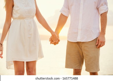 Young couple in love, Attractive man and woman enjoying romantic evening on the beach, Holding hands watching the sunset