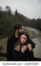 A Young Couple In Love In Black Coats Walks In The Countryside In The Rain. Autumn Gloomy Mood. Cinematic Image