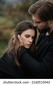 A Young Couple In Love In Black Coats Walks In The Countryside In The Rain. Autumn Gloomy Mood. Cinematic Image