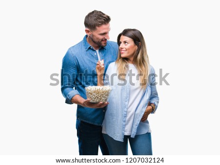 Young couple in love eating popcorn over isolated background with a confident expression on smart face thinking serious