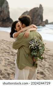 Young couple in love embracing having romantic date on beach, man holding flowers behind his back, giving gift to his girlfriend, vertical shot - Shutterstock ID 2324244729