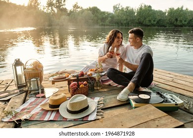 Young couple in love enjoying a glass of wine and a romantic picnic, smiling and looking into each other's eyes.