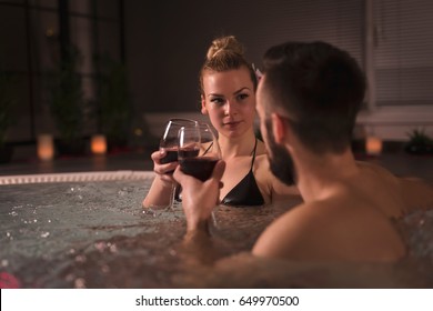 Young couple in love enjoying romantic wellness spa weekend, making a toast with glasses of wine in a jacuzzi bath tub