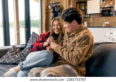 young couple in love fooling around, laughing and fighting over the TV remote control while sitting on sofa