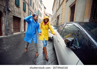 A Young Couple In Love Is Getting Away To A Car While Having A Walk The City In Raincoats In A Cheerful Atmosphere During A Rainy Day. Walk, Rain, City, Relationship