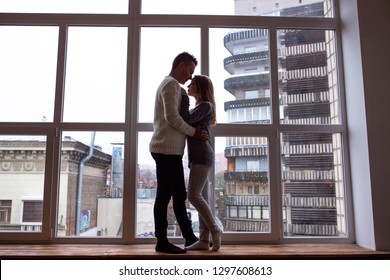 Young couple in love have fun and hugging while standing on window sill at home
