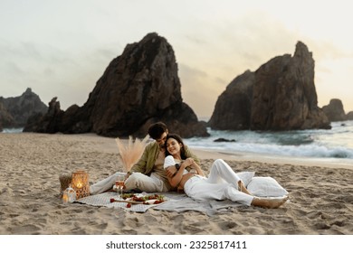 Young couple in love having romantic picnic at the beach, embracing and lying on blanket, celebraing engagement or anniversary. Romance, dating and love concept - Powered by Shutterstock