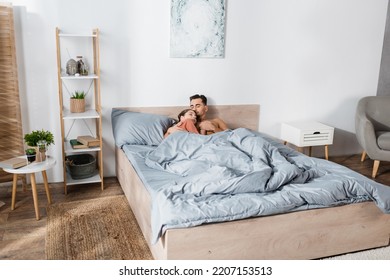 Young Couple In Love Holding Hands While Sleeping Under Grey Blanket In Modern Bedroom