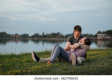 Young Couple In Love Laying On The Grass By The Lake, Cuddling.