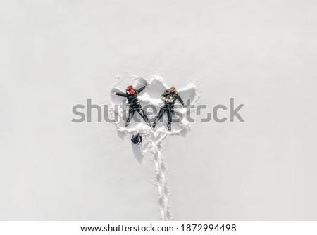 Young couple in love makes snow angels. Snowy white background. Winter, man and woman having fun. Nature parks. Happy girl. Drone, photo from a height.