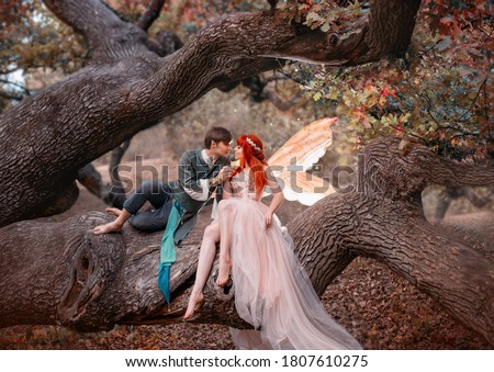 Young couple in love. A man and a woman are hugging on huge tree. Themed creative wedding bright fantasy photography. Fairy woman in long pink dress with bright golden wings. A man in an elf costume