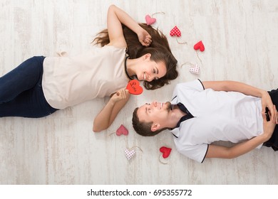 Young couple in love moving in new apartment, lying on floor next to each other with red hearts, and making plans for their future, top view