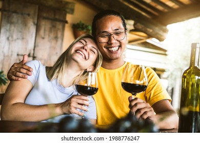 Young Couple In Love On A Date Having Fun Drinking Red Wine In Farmhouse Garden - Multiracial Boyfriend And Girlfriend Enjoying Wine Tasting Weekend Experience At Restaurant Patio - Focus On Guy Face