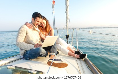 Young couple in love on sail boat having fun remote working at laptop- Happy luxury lifestyle on yacht sailboat - Technology concept with influencer travel blogger - Warm afternoon color tone filter