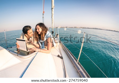 Young couple in love on sail boat having fun with tablet - Happy luxury lifestyle on yacht sailboat - Technology interaction with satellite wifi connection - Round horizon from fisheye lens distortion