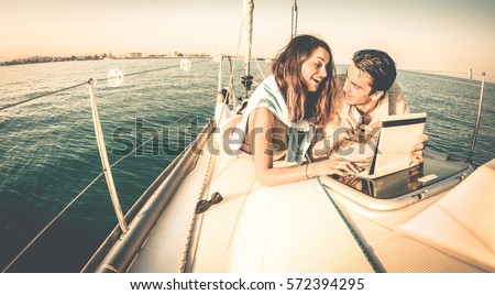 Young couple in love on sail boat having fun with tablet - Happy luxury lifestyle on yacht sailboat - Always connected people interacting with satellite wifi connection - Warm retro contrast filter