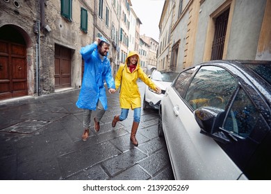 A young couple in love reached a car while having a walk the city in raincoats in a cheerful atmosphere during a rainy day. Walk, rain, city, relationship - Powered by Shutterstock