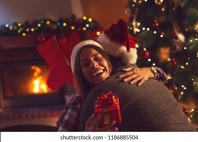 Young couple in love sitting by the fireplace and nicely decorated Christmas tree, exchanging Christmas presents - Powered by Shutterstock